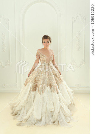 Fashion portrait of beautiful elegant woman in gold dress standing in white interior 106915220