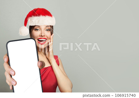 Christmas surprised woman in Santa hat holding smartphone with empty blank display screen 106915740