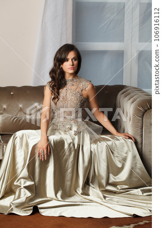 Attractive brunette woman in perfect silver gown. Nice female model sitting on armchair Attractive brunette woman in perfect silver gown. Nice female model sitting on armchair 106916112