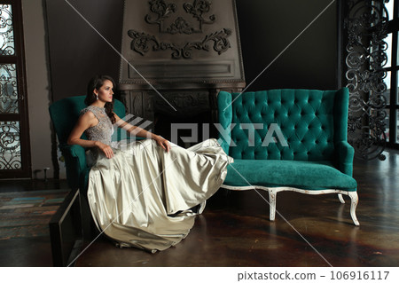 Young gorgeous woman wearing silver evening gown sitting in hotel room. Vogue style model Young gorgeous woman wearing silver evening gown sitting in hotel room. Vogue style model 106916117