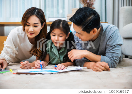Asian family lying on floor painting with little child daughter in living room, Happy Father Mother and daughter drawing together on paper at home, Loving family activity enjoy 106916927