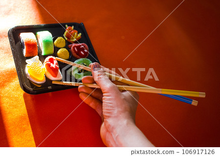 Sushi set on red table, chopsticks in woman's hand, tasting new culinary masterpieces. Asian cuisine of China, Japan. Cooking and eating food for fun. Japanese or Chinese restaurant. Haute cuisine. Sushi set on red table, chopsticks in woman's hand, tasting new culinary masterpieces. Asian cuisine of China, Japan. Cooking and eating food for fun. Japanese or Chinese restaurant. Haute cuisine. 106917126