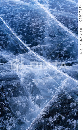 Transparent dark blue ice of frozen Baikal lake with white cracks pattern. Beautiful winter nature background with copy space. 106917174