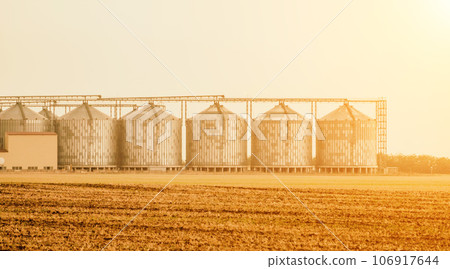 Silos and granary elevator. Modern agro-processing manufacturing plant with grain-drying complex. processing, drying, cleaning, and storing agricultural products in wheat, rye or corn fields Silos and granary elevator. Modern agro-processing manufacturing plant with grain-drying complex. processing, drying, cleaning, and storing agricultural products in wheat, rye or corn fields 106917644