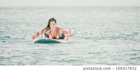 Sea woman sup. Silhouette of happy young woman in pink bikini, surfing on SUP board, confident paddling through water surface. Idyllic sunset. Active lifestyle at sea or river. 106917652