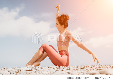 Middle aged well looking woman with black hair, fitness instructor in leggings and tops doing stretching and pilates on yoga mat near the sea. Female fitness yoga routine concept. Healthy lifestyle 106917707