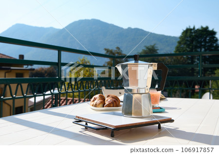 Still life with Italian percolator, moka brewer on the white table in the terrace against Alps background. Copy ad space Still life with Italian percolator, moka brewer on the white table in the terrace against Alps background. Copy ad space 106917857