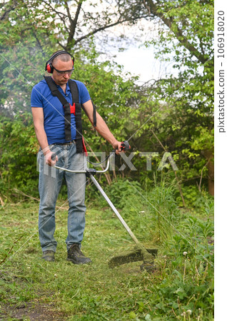 Man mowing tall grass with petrol lawn trimmer vertical photo Man mowing tall grass with petrol lawn trimmer vertical photo 106918020