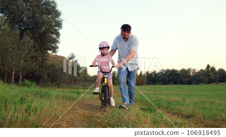 Careful father teaches little girl to ride bicycle in wild summer park 106918495