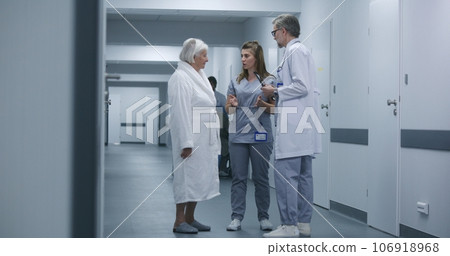 Doctor comes to nurse and elderly woman in clinic corridor Doctor comes to nurse and elderly woman in clinic corridor 106918968
