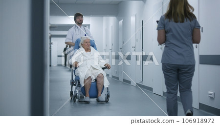 Female doctor comes to colleague and elderly patient in clinic corridor Female doctor comes to colleague and elderly patient in clinic corridor 106918972