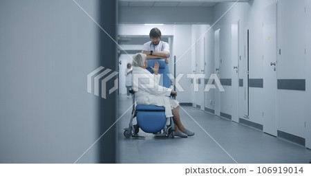Male doctor stands with female patient in wheelchair in clinic corridor Male doctor stands with female patient in wheelchair in clinic corridor 106919014