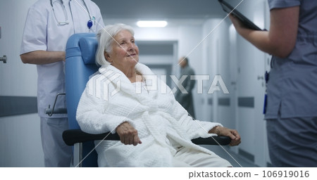 Elderly woman in wheelchair talks to doctor in clinic corridor Elderly woman in wheelchair talks to doctor in clinic corridor 106919016