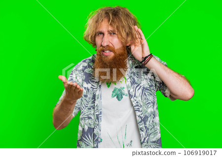 Young man trying hear you looking confused and frowning, keeping arm near ear for louder voice Young man trying hear you looking confused and frowning, keeping arm near ear for louder voice 106919017