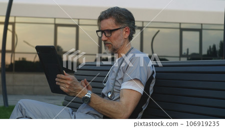 Doctor sits on bench, talks to patient about treatment using digital tablet 106919235