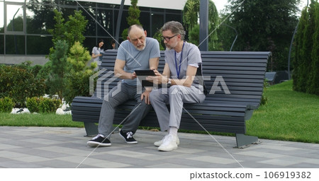 Mature doctor consults elderly patient on bench Mature doctor consults elderly patient on bench 106919382