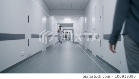 Woman goes medical center corridor, talks to African American doctor Woman goes medical center corridor, talks to African American doctor 106919396