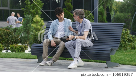 Mature doctor sits with adult patient on bench Mature doctor sits with adult patient on bench 106919397