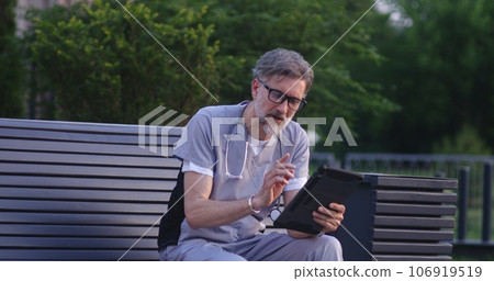 Doctor in uniform sits on bench, talks to patient using digital tablet 106919519