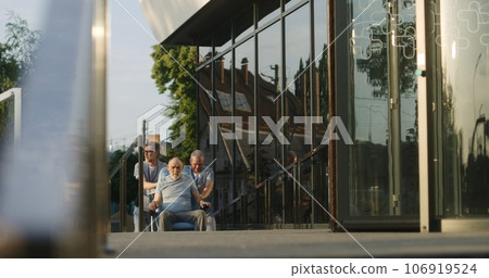 Two doctors take elderly man with disability to the clinic Two doctors take elderly man with disability to the clinic 106919524