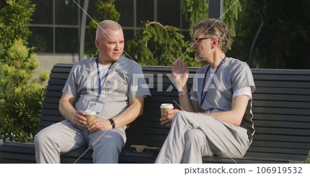 Two male doctors sit on bench and drink coffee Two male doctors sit on bench and drink coffee 106919532
