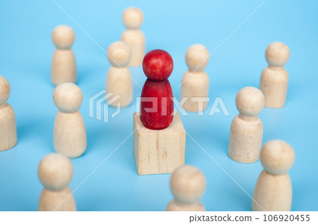 Red figure on top of wooden cube surrounded with other wooden figure. Red figure on top of wooden cube surrounded with other wooden figure. 106920455
