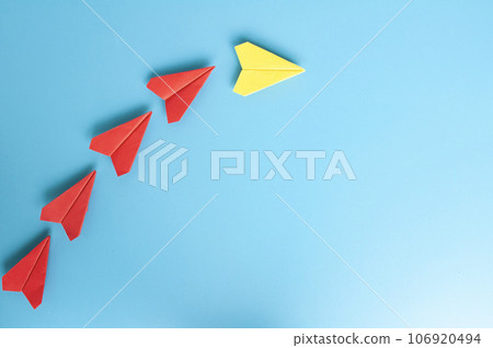 Top view of yellow paper airplane origami leading red paper airplanes on blue cover background Top view of yellow paper airplane origami leading red paper airplanes on blue cover background 106920494