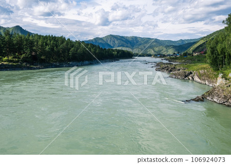 A wide, full-flowing mountain river with a fast current. Large stones stick out of the water. The large turquoise-colored mountain river Katun in the Altai Mountains, Altai Republic. A wide, full-flowing mountain river with a fast current. Large stones stick out of the water. The large turquoise-colored mountain river Katun in the Altai Mountains, Altai Republic. 106924073