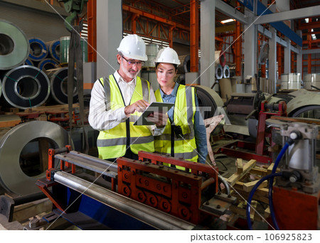 Two worker standing amidst the humming machinery of a bustling factory. Discover the essence of teamwork, innovation and precision as these skilled individuals navigate the industrial landscape. 106925823