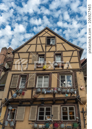 Facade of a traditional Alsatian house decorated with old watering cans in the city center. 106927465
