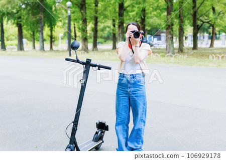 A woman taking pictures with a camera while traveling on an electric kickboard A woman taking pictures with a camera while traveling on an electric kickboard 106929178