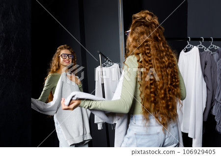 Young curly woman choosing clothes at fitting room. Shopping concept 106929405