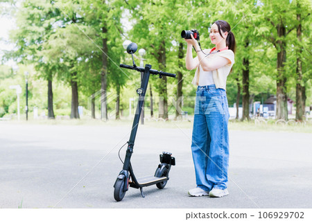 A woman taking pictures with a camera while traveling on an electric kickboard A woman taking pictures with a camera while traveling on an electric kickboard 106929702
