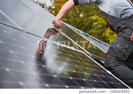 Man technician mounting photovoltaic solar panels on roof of house. Close up view of engineer installing solar module system with help of hex key. Concept of alternative, renewable energy. 106929982