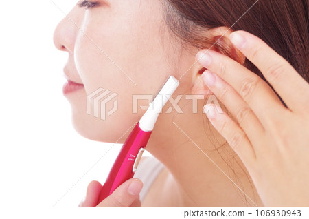 A woman removing unwanted facial hair with an electric trimmer 106930943
