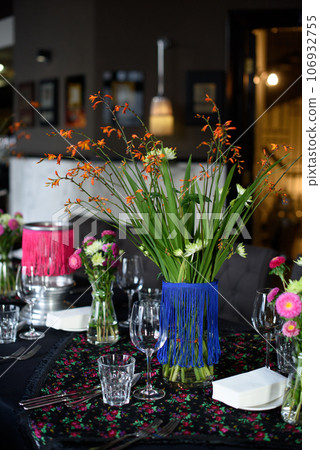 Glasses, flowers, fork, flowers, knife served for dinner in restaurant with cozy interior Glasses, flowers, fork, flowers, knife served for dinner in restaurant with cozy interior 106932755