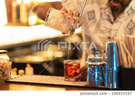 The bartender mixes the cocktail and pouring it into the glass The bartender mixes the cocktail and pouring it into the glass 106933587