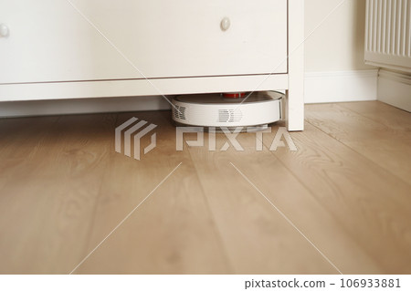 Wireless autonomous robotic vacuum cleaner vacuums with brushes under commode at living room. Self-propelled cleaning robot. Household remote control appliances. Smart cleaning technology. 106933881