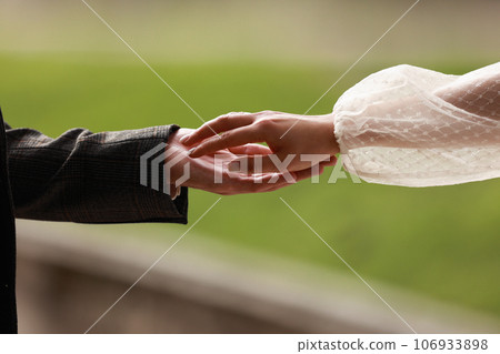 Hands of bride in white dress and groom in suit reaching each other, touching fingers on green background. Helping hands for save and support people concept. Wedding day. Valentine day. Hands of bride in white dress and groom in suit reaching each other, touching fingers on green background. Helping hands for save and support people concept. Wedding day. Valentine day. 106933898