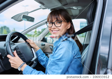 Middle-aged woman driver sitting behind wheel in car, smiling looking at camera Middle-aged woman driver sitting behind wheel in car, smiling looking at camera 106933912
