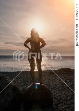 Woman summer travel sea. A happy tourist enjoys taking pictures of her travels, posing by an old, rusty sea mine on a beach surrounded by volcanic mountains, sharing travel adventure journey 106933994