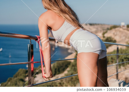 Fitness woman sea. Outdoor workout with fitness rubber bands in park over beach. Female fitness yoga routine concept. Healthy lifestyle. Happy fit woman exercising with rubber band in park. Fitness woman sea. Outdoor workout with fitness rubber bands in park over beach. Female fitness yoga routine concept. Healthy lifestyle. Happy fit woman exercising with rubber band in park. 106934039
