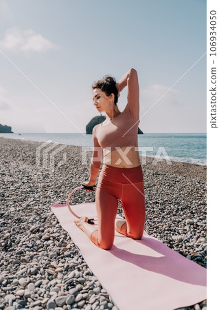 Woman sea pilates. Sporty happy middle aged woman practicing fitness on beach near sea, smiling active female training with ring on yoga mat outside, enjoying healthy lifestyle, harmony and meditation Woman sea pilates. Sporty happy middle aged woman practicing fitness on beach near sea, smiling active female training with ring on yoga mat outside, enjoying healthy lifestyle, harmony and meditation 106934050