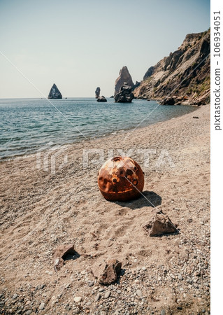 Old rusty round floating marine mines on the beach with rocky shore and sea background. Pollution, nature protection, war and peace concept. Old rusty round floating marine mines on the beach with rocky shore and sea background. Pollution, nature protection, war and peace concept. 106934051