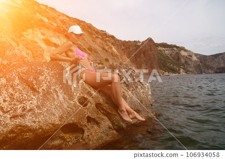 Woman travel sea. Pink bikini tourist captures sea memory, posing on beach amidst volcanic mountains for travel adventure. Happy woman enjoys outdoor photography. Woman travel sea. Pink bikini tourist captures sea memory, posing on beach amidst volcanic mountains for travel adventure. Happy woman enjoys outdoor photography. 106934058