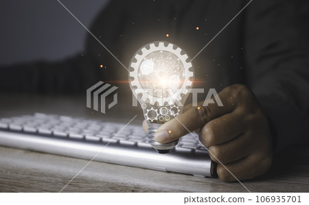 Man holding a bright light bulb with gear icon and using laptop computer. 106935701
