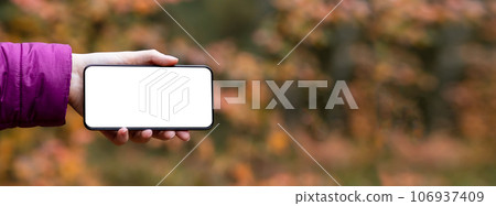 Hand holding mobile phone, horizontal screen mockup on autumn banner background Hand holding mobile phone, horizontal screen mockup on autumn banner background 106937409