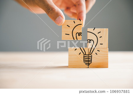 Hand holding a wooden cube with light bulb icon, symbolizing idea and creativity concept. Light background with copy space. Teamwork brainstorming, evaluating innovative ideas for business development 106937881