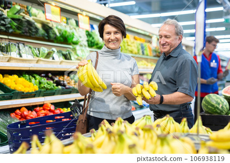 Elderly man and a woman choose bananas in the store Elderly man and a woman choose bananas in the store 106938119