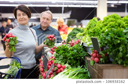 Elderly woman chooses radish in vegetable and fruit department Elderly woman chooses radish in vegetable and fruit department 106938162